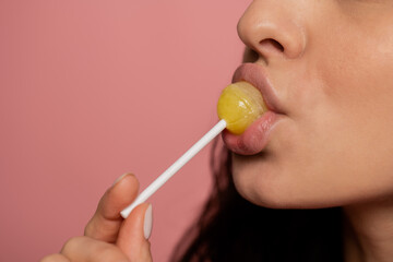 Young lady with sensual plump lips sucking a tasty yellow sweet round lollipop on a white plastic stick. Self-indulgence concept