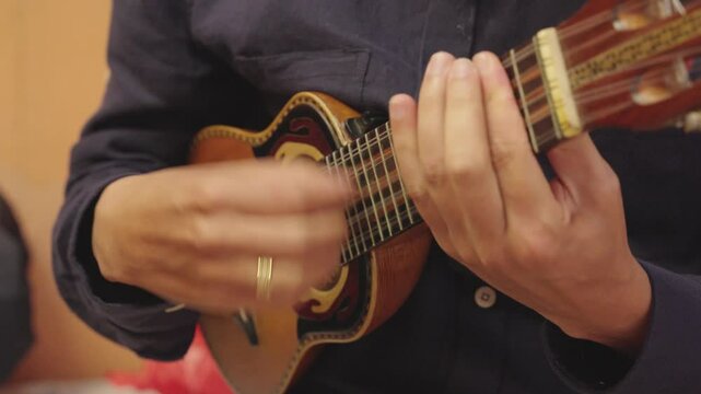 Close-up of a person playing a charango, a small Andean stringed instrument. The focus is on the musician's hands and the instrument.