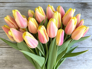 A bouquet of delicate pastel-colored tulips lies on a wooden table. Realistic spring still life.
