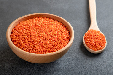 Red lentil grains in a wooden bowl and spoon on a gray background. Top view of dried orange lentils inside the bow