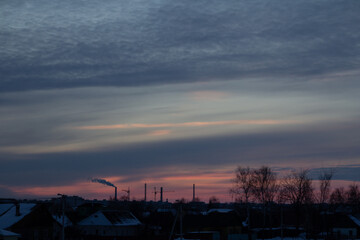 Industrial pipes silhouetted against a vibrant sunset sky, blending nature with urban industry.