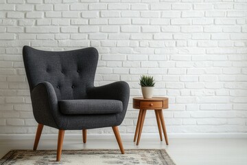 A gray armchair with wooden legs sits on a rug in front of a white brick wall with a small wooden side table and plant
