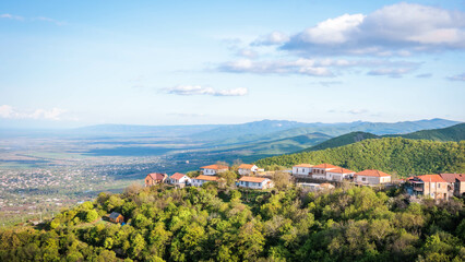 Picturesque view of Sighnaghi town in Kakheti, Georgia, with red-roofed houses surrounded by green hills and panoramic Alazani Valley in the distance