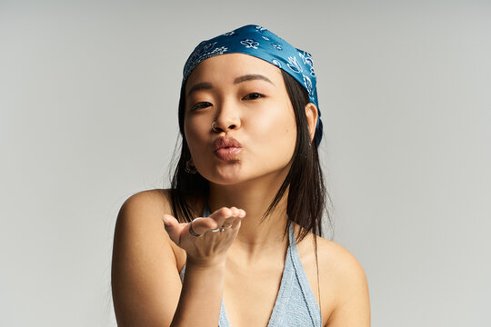 Joyful young woman blowing kisses with a playful smile against a neutral background