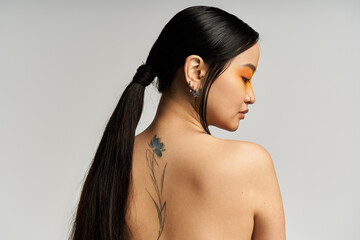 Young beautiful asian woman displaying a floral tattoo in an elegant hairstyle with artistic makeup