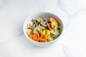 colorful farfalle pasta in a bowl on white marble background