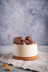 Milk chocolate candies with nut filling in a speckled beige ceramic bowl. Light background, textile, and walnuts create a cozy composition.