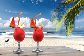 two red drinks with melon garnish on a tropical beach