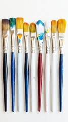 Fototapeta premium Set of ten paintbrushes with colorful bristles arranged in a row against a white background, showcasing various sizes and types for artistic painting projects