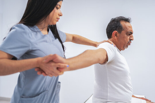 Female physiotherapist helping mature man with shoulder exercises for rehabilitation and pain relief