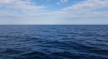 Obraz premium A view of the open ocean under a partly cloudy sky with gentle waves on the water surface visible