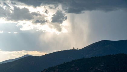 Rain falling over a mountain ridge under thick storm clouds as sunlight breaks through in the distance
