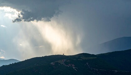 Fototapeta premium Rain falling over a mountain ridge under thick storm clouds as sunlight breaks through in the distance