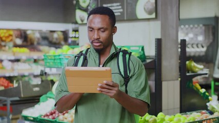 African american young delivery man using digital tablet pc waiting customer order pickingup food in grocery store supermarket.