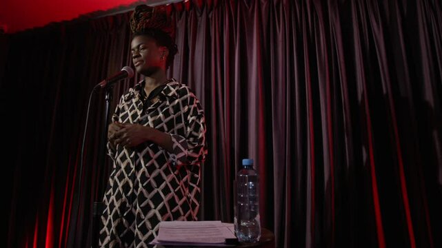 Low angle slow motion shot of African American woman giving emotional stand-up performance on dimly lit stage