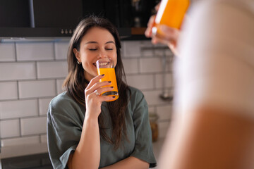 Fototapeta premium Young woman smiling and drinking fresh orange juice in the kitchen 