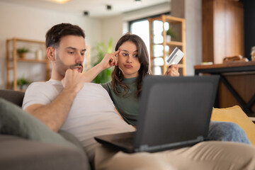 Couple thinking while shopping online with laptop
