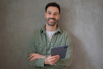 Smiling man holding a tablet against gray wall