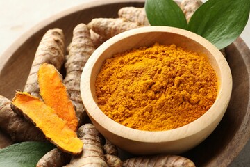 Aromatic turmeric powder in bowl, fresh roots and leaves on light grey table, closeup
