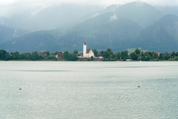 Serene lakeside view with mountains in the background near a quiet village during overcast weather