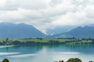Mountain landscape with serene lake reflecting cloudy sky and lush greenery in the foreground at...