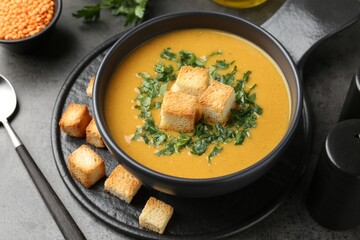 Delicious lentil cream soup served with croutons on grey table, closeup