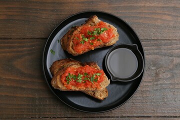 Tasty bread with tomatoes, parsley and oil on wooden table, top view