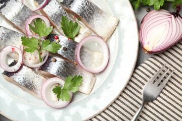 Pieces of delicious herring with spices and onions served on table, closeup