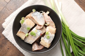 Pieces of delicious herring with green onions on wooden table, top view