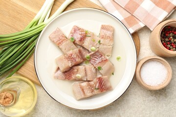 Pieces of delicious herring with green onions on light table, flat lay