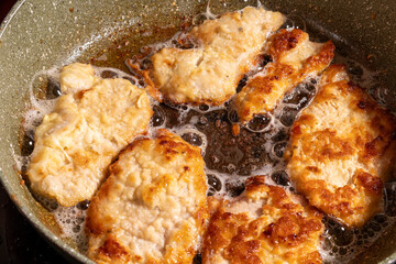Golden brown breaded chicken pieces sizzle in a pan of hot oil, with bubbles forming around them.