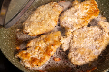 Four golden-brown breaded chicken pieces sizzling in bubbling oil inside a pan with a speckled surface.