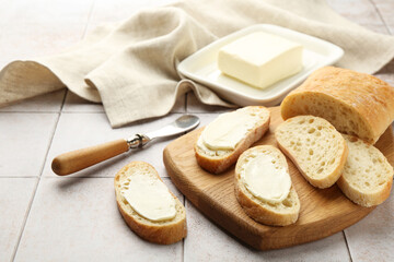 Pieces of bread with butter and knife on light tiled table