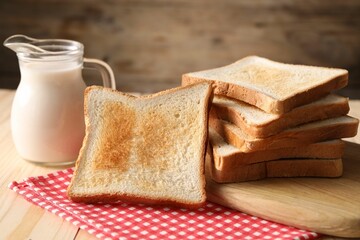 Slices of tasty toasted bread and jug of milk on wooden table, closeup