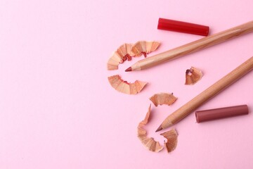 Lip pencils and shavings on light pink background, flat lay. Space for text