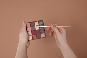 Woman with eyeshadow palette and brush on beige background, closeup