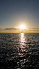 The sun is setting over the ocean, casting a warm glow on the water. The sky is a deep blue, with a few clouds scattered throughout. The scene is peaceful and serene, with the water