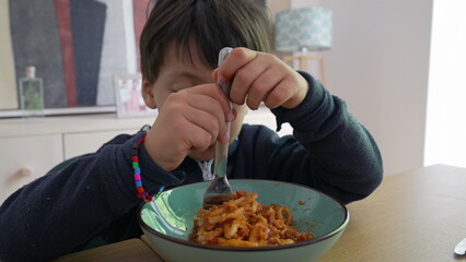 Child twirling spaghetti with a fork, gripping it tightly while intensely focused on the meal, highlighting the effort and engagement in self-feeding within a familiar home environment-SD 480p