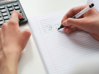 A student doing math in a notebook using a calculator. Close up.