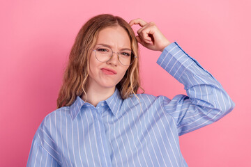 Young woman with glasses making a puzzled expression, wearing a striped blue shirt against a bright pink background