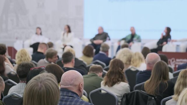 Business professionals attending panel discussion event, seated audience and speakers sharing insights