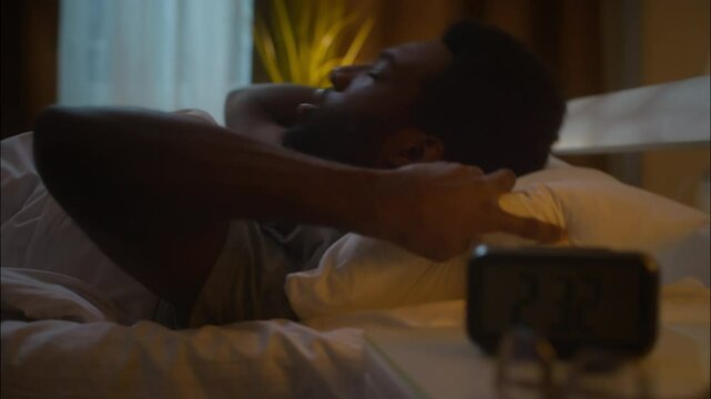 Stressed exhausted African American ethnic man guy male lying on bed suffering insomnia disorder can't sleep awake bad sleeping nap trouble napping stress health problems at home bedroom late night