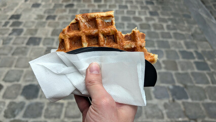 Original bitten Brussels waffle held in hand with crispy texture and golden brown color, perfect for street food lovers and dessert enthusiasts, indulgent snack concept
