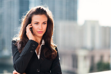 Pretty young businesswoman talking on mobile phone with downtown buildings skyline in background