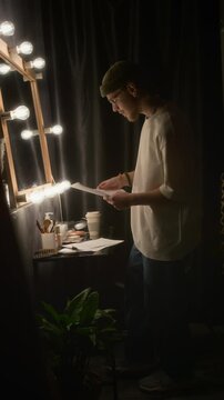 Vertical shot of man looking at himself in mirror and rereading his performance script in dressing room