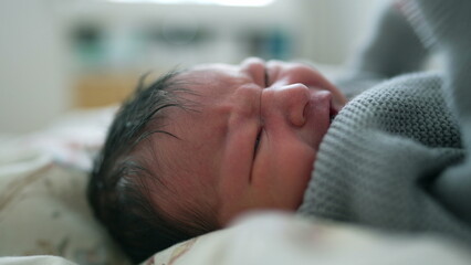 Newborn baby wrapped in a cozy blanket with a frown, showing signs of discomfort, emotional moment...
