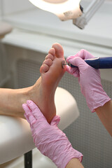 A podiatrist cosmetologist in pink latex gloves cleanses the skin of the client's feet from calluses and corns with a professional tool. Heel polishing, foot polishing procedure. Pedicure room