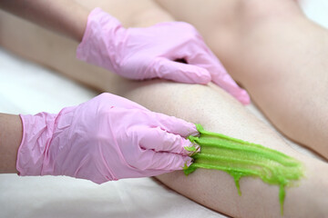 A cosmetologist wearing pink latex gloves removes leg hair. Sugar hair removal foot skin care with liquid sugar. A cosmetologist waxes women's legs at the spa. Female waxing. Epilation by sugaring