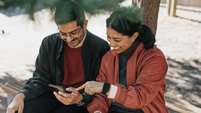 The couple sits outdoors under a tree each wearing a biosensor with the woman pointing at her devices screen both smiles indicating a fun shared learning moment about stress