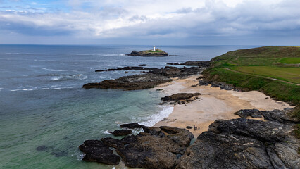 Rugged coastline of South England with towering cliffs, pebble beaches, and a scenic island lighthouse, seen by drone.